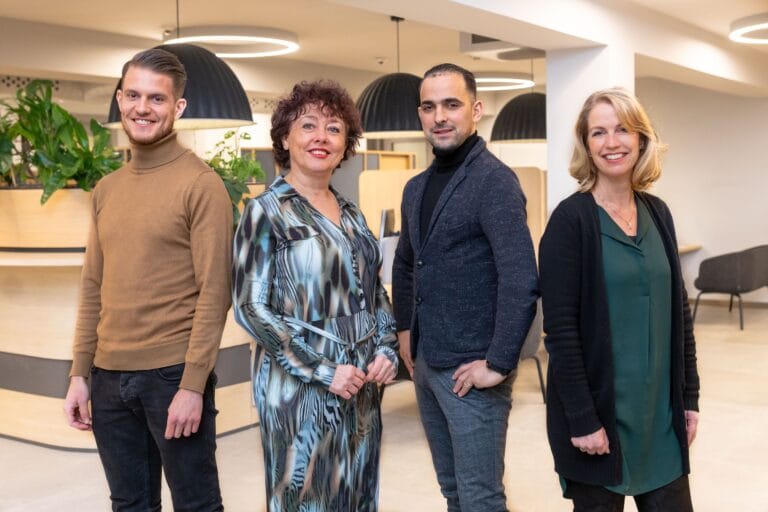 Vier collega’s lachen en poseren voor de foto in de centrale hal